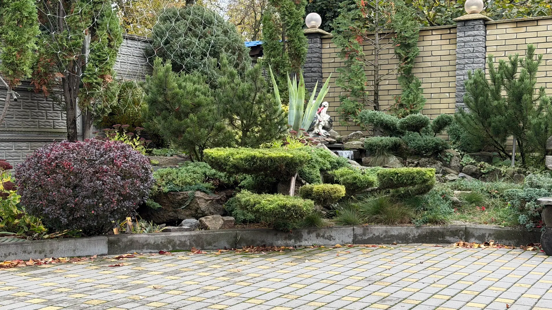 Хвойні рослини та декоративний водоспад біля мощеної доріжки